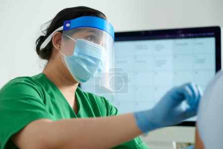 Téléchargez les photos : Infirmière sérieuse portant un écran protecteur et un masque médical lors de l'injection du vaccin dans le bras du patient - en image libre de droit