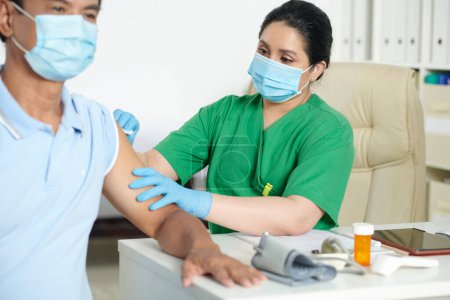 Foto de Enfermera en máscara protectora que limpia el hombro del paciente con una bola de algodón antes de inyectarse la vacuna - Imagen libre de derechos