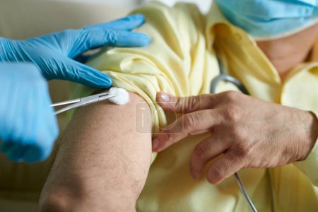 Foto de Enfermera limpiando el lugar de inyección en el brazo del paciente con una bola de algodón antes de vacunarlo contra el coronavirus - Imagen libre de derechos