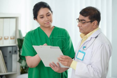 Foto de Enfermera dando portapapeles con historial médico del paciente al médico general - Imagen libre de derechos