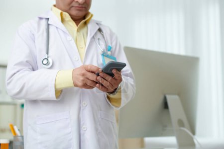 Téléchargez les photos : Image recadrée du médecin répondant aux messages texte du patient sur smartph - en image libre de droit