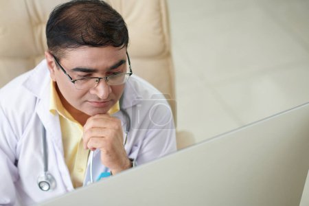 Téléchargez les photos : Le médecin pensif vérifie le document avec les résultats des tests médicaux du patient malade - en image libre de droit