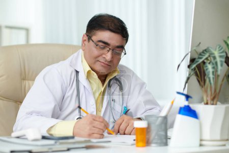 Photo for Experienced chief physician signing documents at his desk - Royalty Free Image