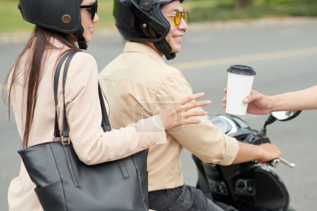 Photo for Drive through worker giving cup of coffee to young woman riding on scooter with boyfriend or colleague - Royalty Free Image