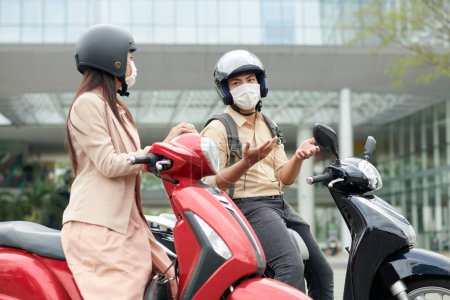Foto de Joven hombre y mujer en scooters hablando cuando están de pie en el atasco de tráfico y esperando la luz verde - Imagen libre de derechos