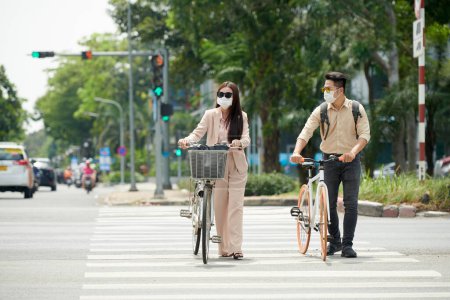 Photo for Citizens wearing sunglasses and medical masks when crossing road with bicycles - Royalty Free Image