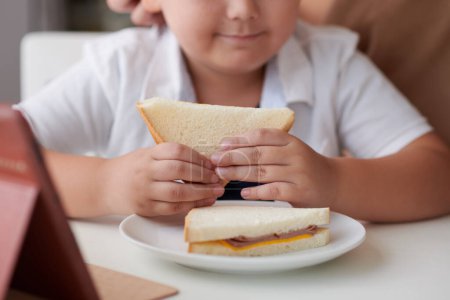 Photo for Cropped image of little boy eating tasty sandwich with ham and cheese - Royalty Free Image