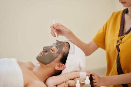 Foto de Esteticista aplicación de abrillantamiento y mascarilla de arcilla hidratante en la cara del cliente femenino - Imagen libre de derechos