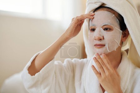 Photo for Young Vietnamese woman applying sheet mask to revitalize dull skin - Royalty Free Image
