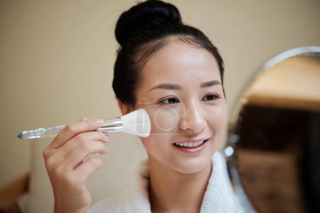 Téléchargez les photos : Sourire jeune femme appliquant fond de teint liquide avec pinceau de maquillage synthétique - en image libre de droit