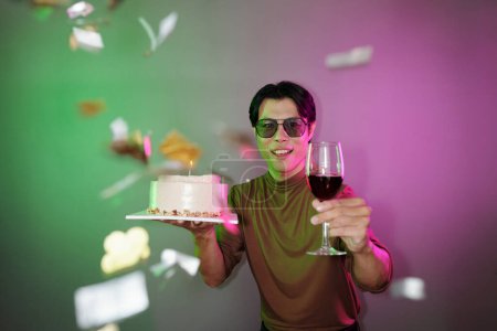 Téléchargez les photos : Joyeux homme avec gâteau d'anniversaire et verre de vin debout sous les confettis tombant - en image libre de droit