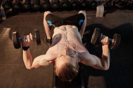 Photo for Athletic shirtless young man doing dumbbell press on inclined bench at gym - Royalty Free Image