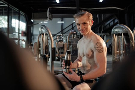 Photo for Portrait of smiling sweaty young man drinking after intense training in gym - Royalty Free Image