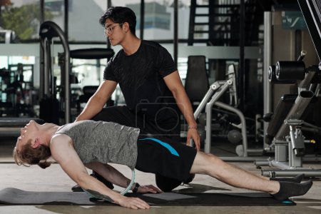 Photo for Fit young man doing wheel-assisted fish pose under control of his trainer - Royalty Free Image