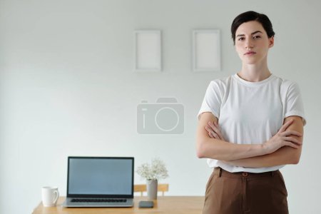 Téléchargez les photos : Confiant ambitieux jeune femme debout au bureau à domicile avec ordinateur portable ouvert - en image libre de droit