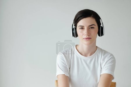 Foto de Retrato de mujer joven en camiseta blanca escuchando podcast o pista de música en auriculares - Imagen libre de derechos