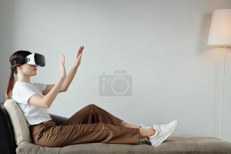 Photo for Young woman relaxing on couch at home and exploring metaverse - Royalty Free Image