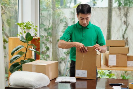 Photo for Young businessman packing orders in cardboard boxes before shipping - Royalty Free Image