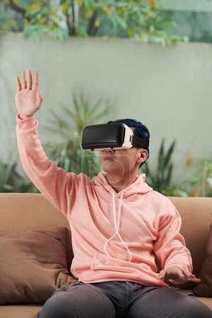 Photo for Young man in pink hoodie playing videogame in VR headset - Royalty Free Image