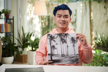 Téléchargez les photos : Joyeux jeune homme créatif montrant une photo en noir et blanc qu'il a faite pour une exposition personnelle - en image libre de droit