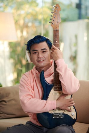 Téléchargez les photos : Portrait de jeune homme créatif souriant aux cheveux bleus posant avec sa guitare électrique - en image libre de droit