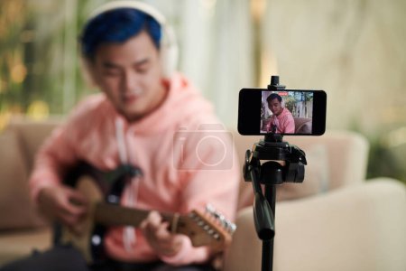 Photo for Talented young man recording himself playing guitar on smartphone - Royalty Free Image