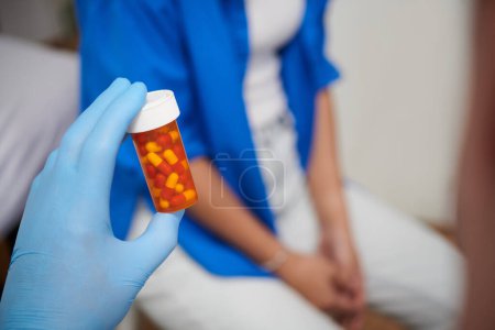 Téléchargez les photos : Main du médecin généraliste en gant de caoutchouc tenant bouteille de pilules prescrites au patient - en image libre de droit
