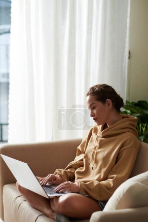 Foto de Mujer joven seria revisando el código de programación en la pantalla del ordenador portátil cuando se trabaja desde casa debido a la pandemia de coronavirus - Imagen libre de derechos