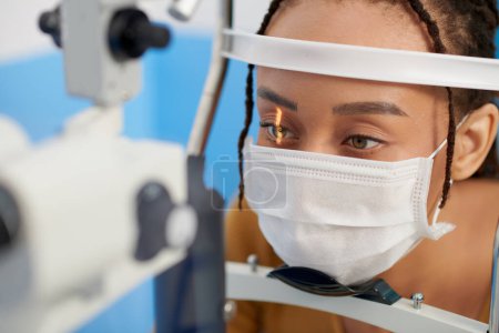 Photo for Female patient in medical mask getting eyes examined with slit lamp, microscope that allows doctor to closely examine the eye - Royalty Free Image