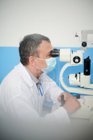 Photo for Ophthalmologist in protective mask examined eyes of patient with modern autorefractometer - Royalty Free Image