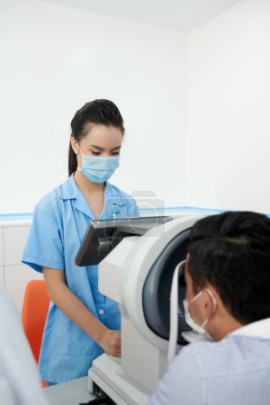 Photo for Serious ophthalmic nurse setting refractometer to check eyesight of patient - Royalty Free Image