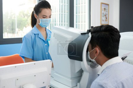 Photo for Young ophthalmic nurse in medical mask checking eyes of patient for various disesases - Royalty Free Image