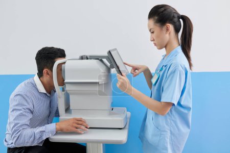 Photo for Young female doctor setting refractometer machine to check eyes of patient before vision correction surgery - Royalty Free Image