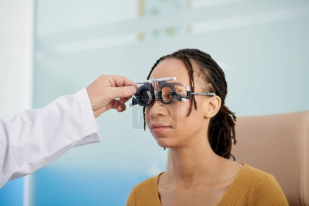 Photo for Ophthalmologist using adjustable optical trial lens frame to measure distance between eyes of patient - Royalty Free Image