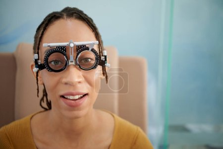Photo for Portrait of smiling Black woman wearing adjustable optical trial lens frame when reading letters on chart - Royalty Free Image