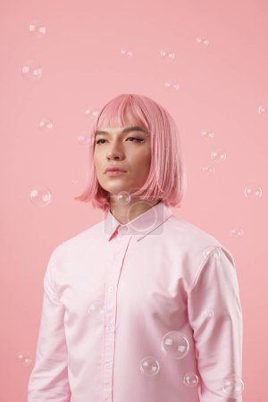 Photo for Portrait of young Asian man with beautiful eye look and pink bob haircut standing under falling soap bubbles - Royalty Free Image