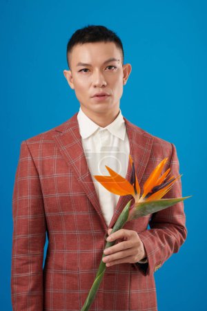 Foto de Retrato de hombre joven en color óxido chaqueta a cuadros sosteniendo flor pájaro del paraíso flor - Imagen libre de derechos