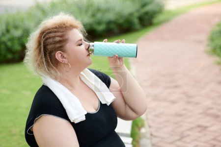 Photo for Curvy stylish young woman drinking fresh water after jogging or working out in park - Royalty Free Image