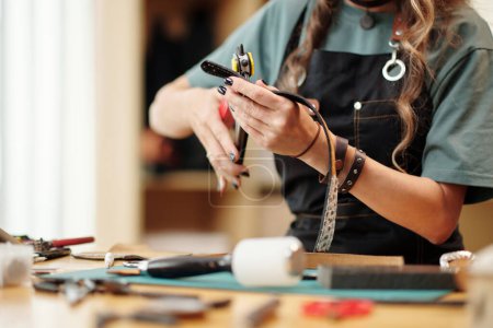 Téléchargez les photos : Femme utilisant un outil de poinçonnage rotatif pour faire des trous dans la ceinture en cuir - en image libre de droit