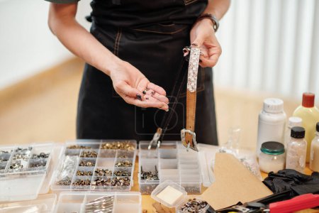 Téléchargez les photos : Image rapprochée d'un artisan choisissant des oeillets pour sa ceinture en cuir - en image libre de droit