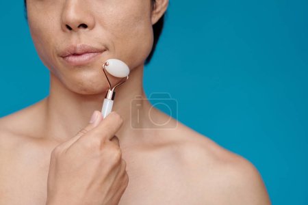 Photo for Cropped image of man massaging chin with quartz roller, isolated on blue - Royalty Free Image