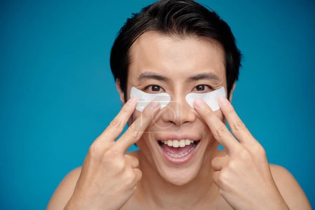 Photo for Excited man applying brightening undereye patches when getting ready - Royalty Free Image