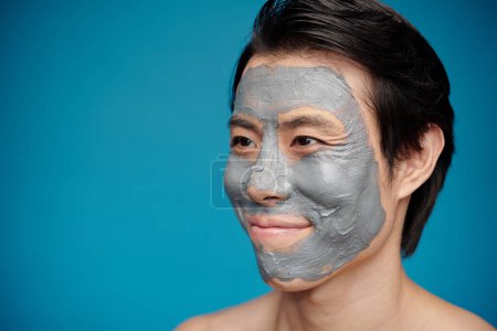 Téléchargez les photos : Portrait d'homme heureux avec masque d'argile hydratante sur le visage - en image libre de droit