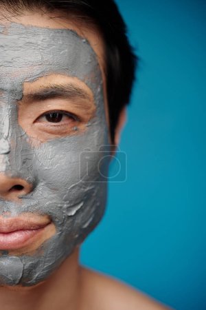 Photo for Half face of smiling man with clay beauty treatment on face looking at camera - Royalty Free Image