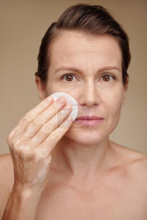 Photo for Portrait of mature woman applying toner to gently refresh skin - Royalty Free Image