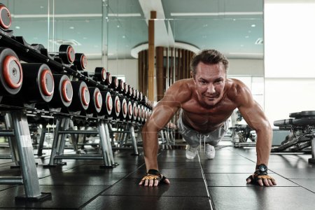 Photo for Strong fit man doing push-up on gym floor when working on chest muscles - Royalty Free Image