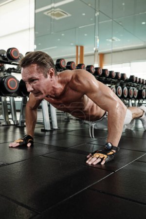 Foto de Hombre fuerte usando smartwatch al hacer flexiones en el gimnasio - Imagen libre de derechos