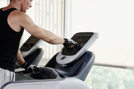 Téléchargez les photos : Homme mûr fixant la vitesse sur le tapis roulant lors de l'exercice dans la salle de gym - en image libre de droit
