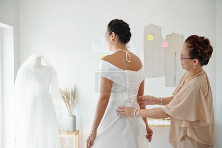 Photo for Mother helping daughter to tighten corset on wedding dress - Royalty Free Image