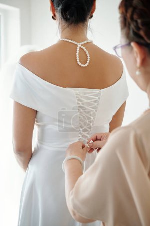 Foto de Elegante novia pidiendo a la madre que apriete el corsé en el vestido de novia - Imagen libre de derechos